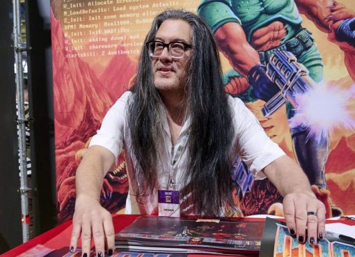 John Romero at a convention with Doom artwork in the background, id Software co-founder