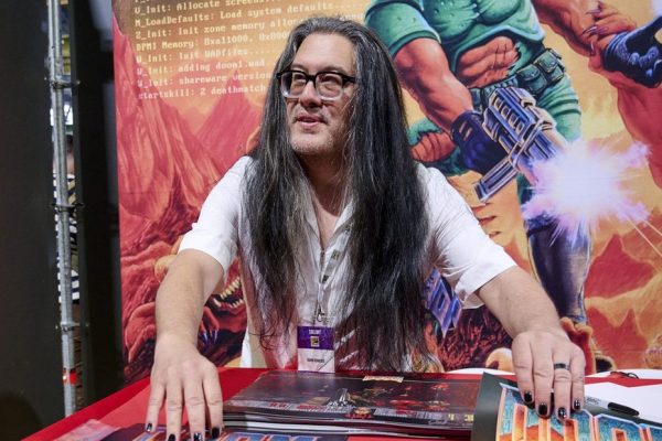 John Romero at a convention with Doom artwork in the background, id Software co-founder