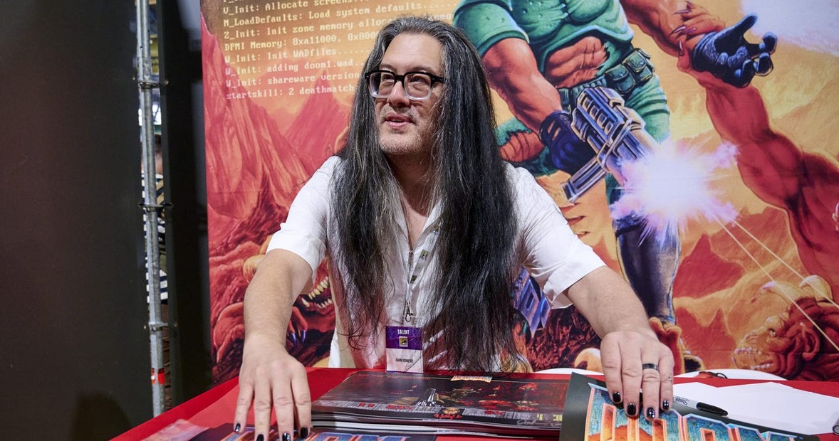 John Romero at a convention with Doom artwork in the background, id Software co-founder