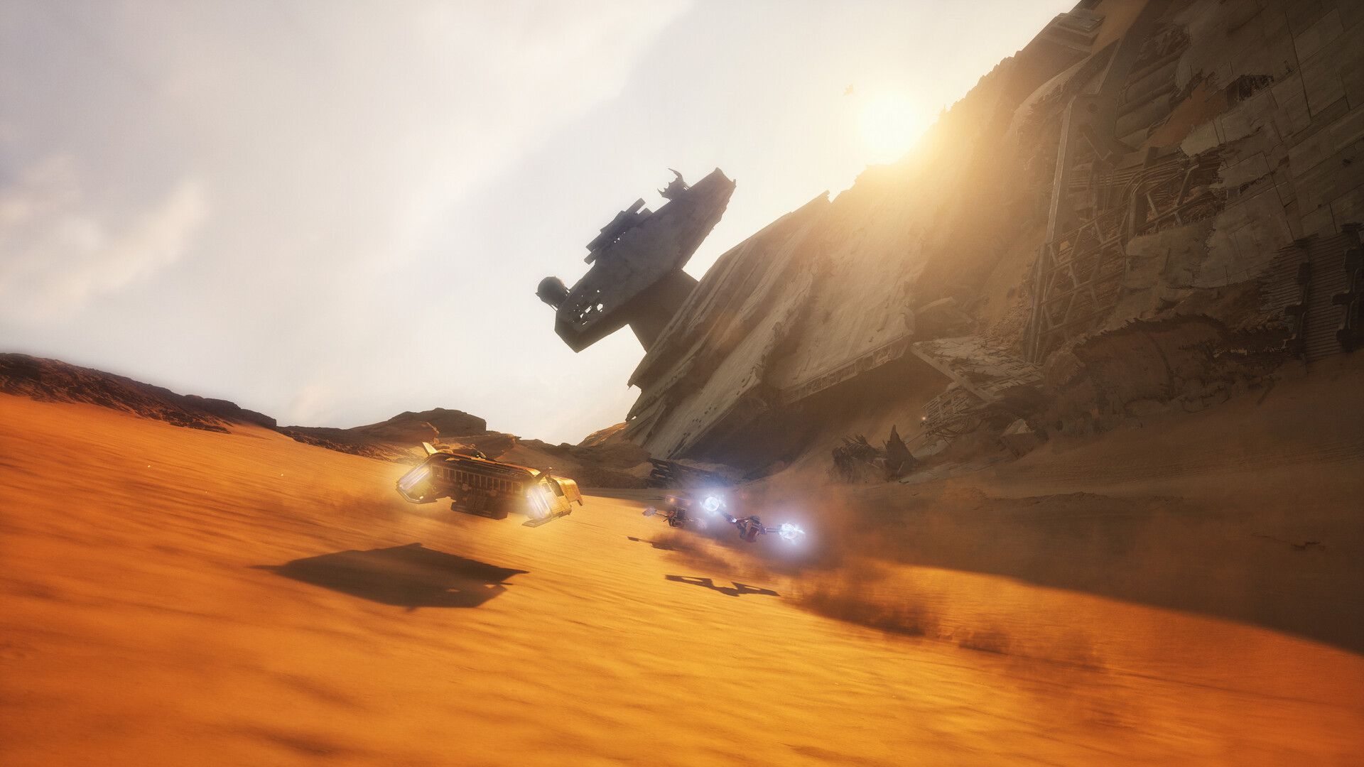 Speeders race across a desert dune beneath the wreckage of a crashed Star Destroyer